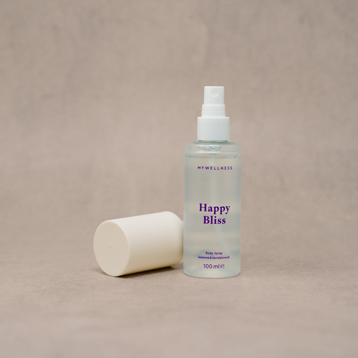 Happy Bliss Body Spray von MyWellness mit abgenommener Kappe vor beigem Hintergrund