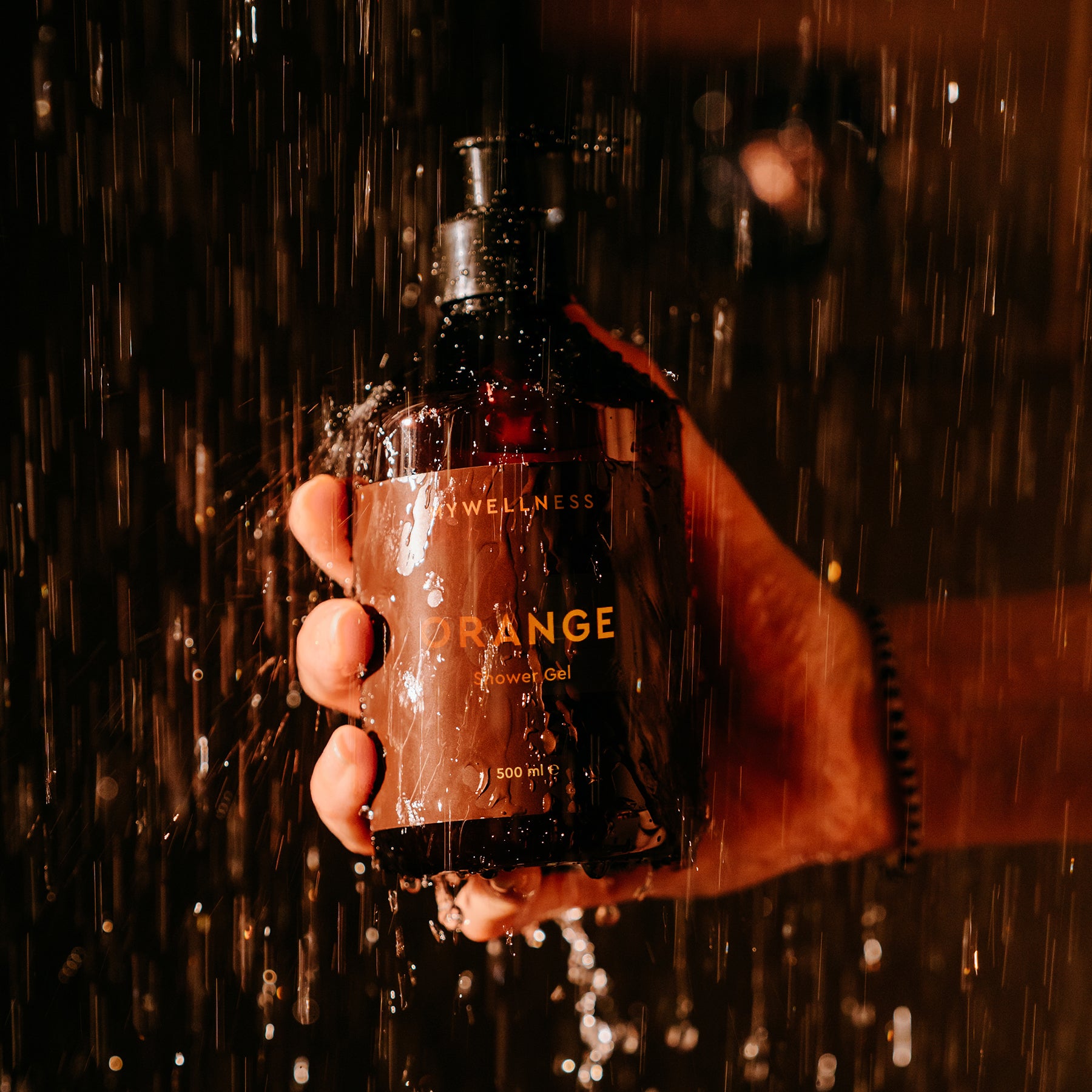Person hält schäumende Bottle des Shower Gel Orange von MyWellness unter warmem Wasser in der Dusche