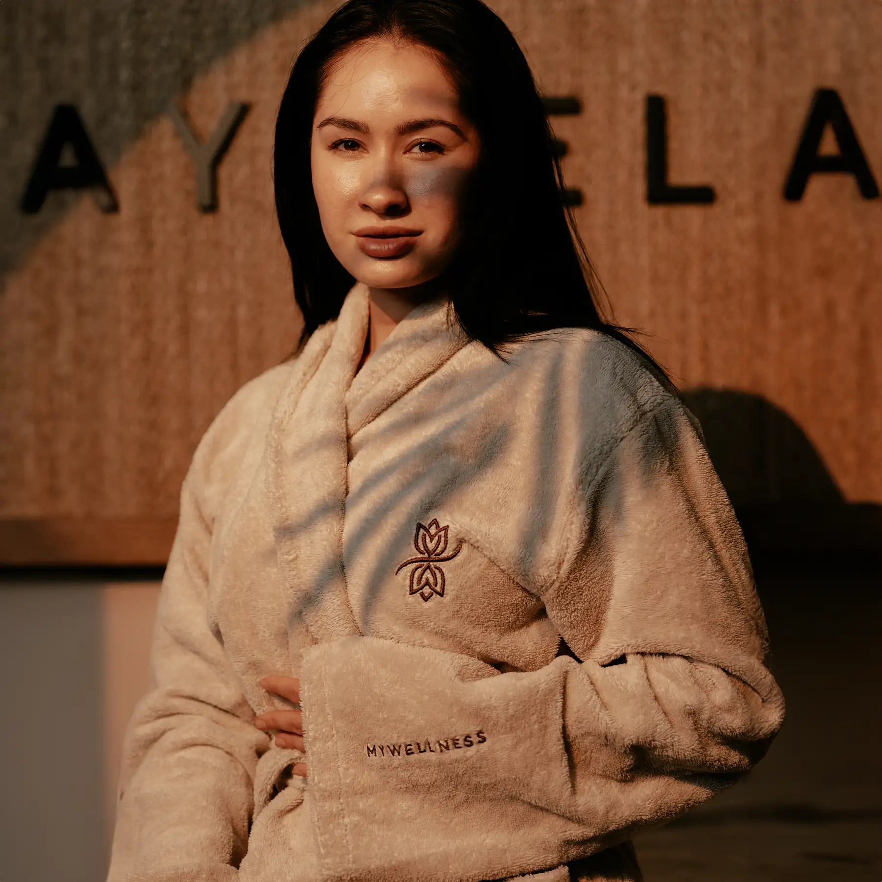 Frau trägt beigen MyWellness Bademantel – luxuriöser Wellness-Bademantel mit Stickerei, aufgenommen im warmen Abendlicht