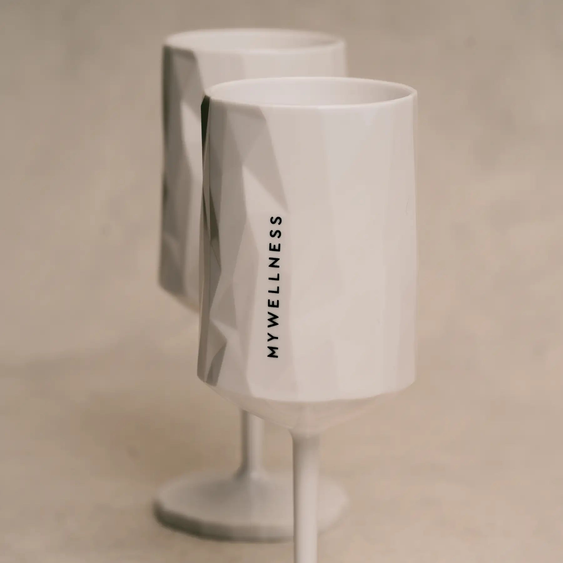 Zwei moderne weiße MYWELLNESS-Weingläser mit sichtbarem Logo und strukturierter Oberfläche, elegante Studioaufnahme.