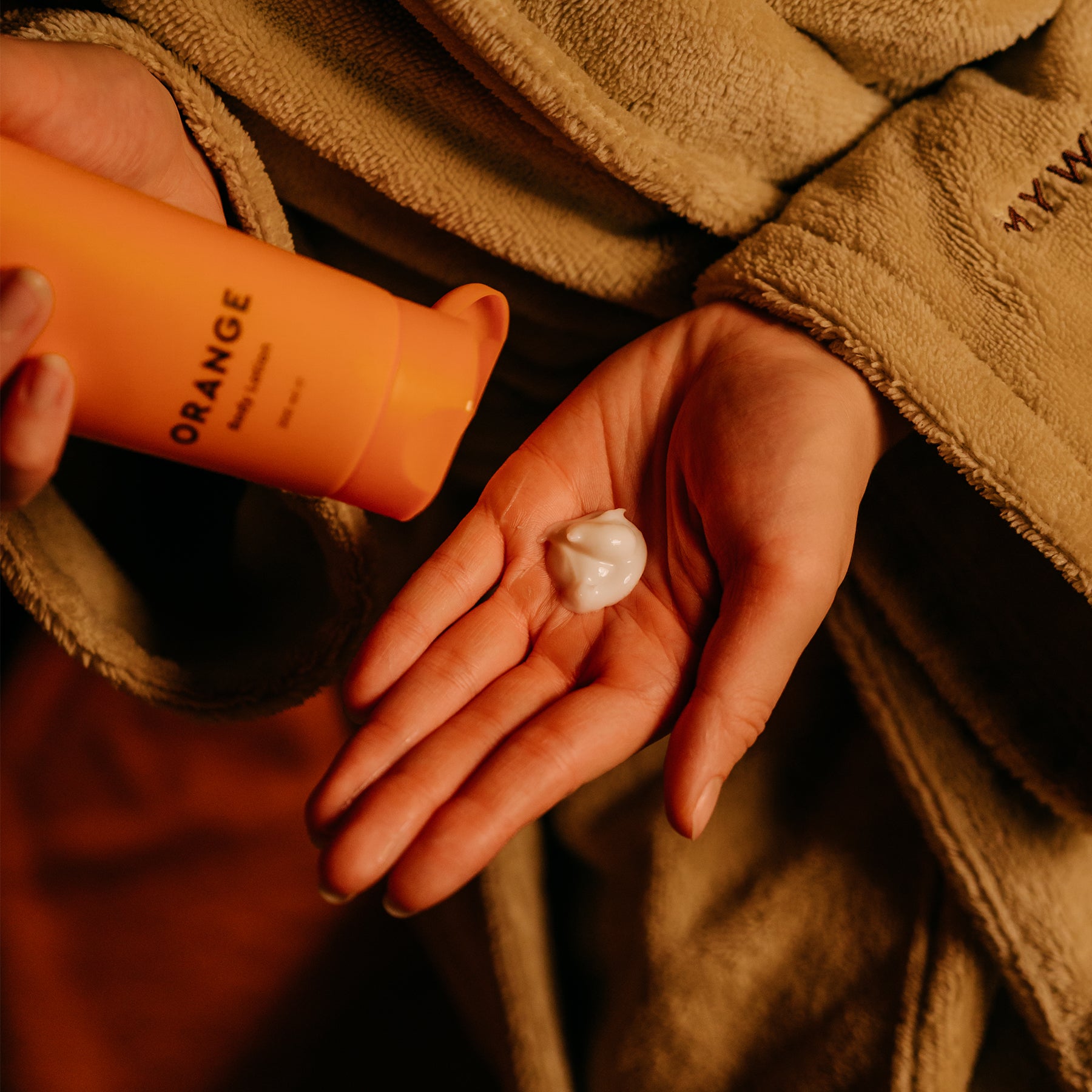 Person trägt MyWellness Bodylotion Orange auf die Haut auf in warmer Wellness-Atmosphäre