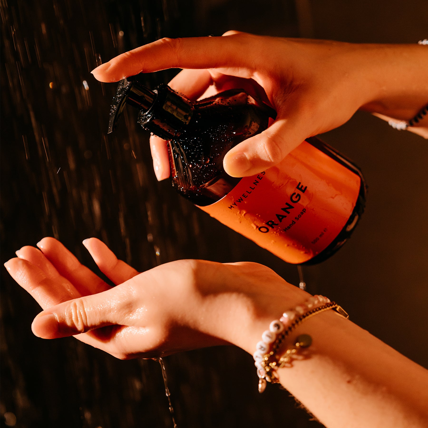 Hände dosieren die Hand Soap Orange aus dem Pumpspender während der Anwendung im Badezimmer.