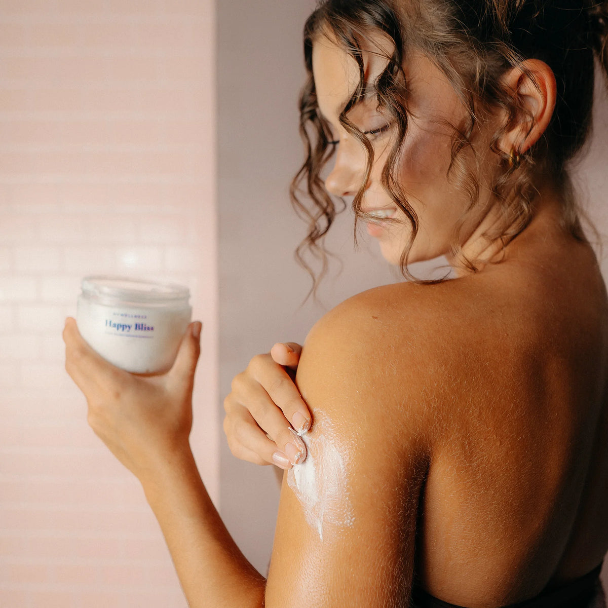 Frau trägt Happy Bliss Shower Mousse mit Jasmin und Sandelholz in der Dusche auf den Oberarm auf