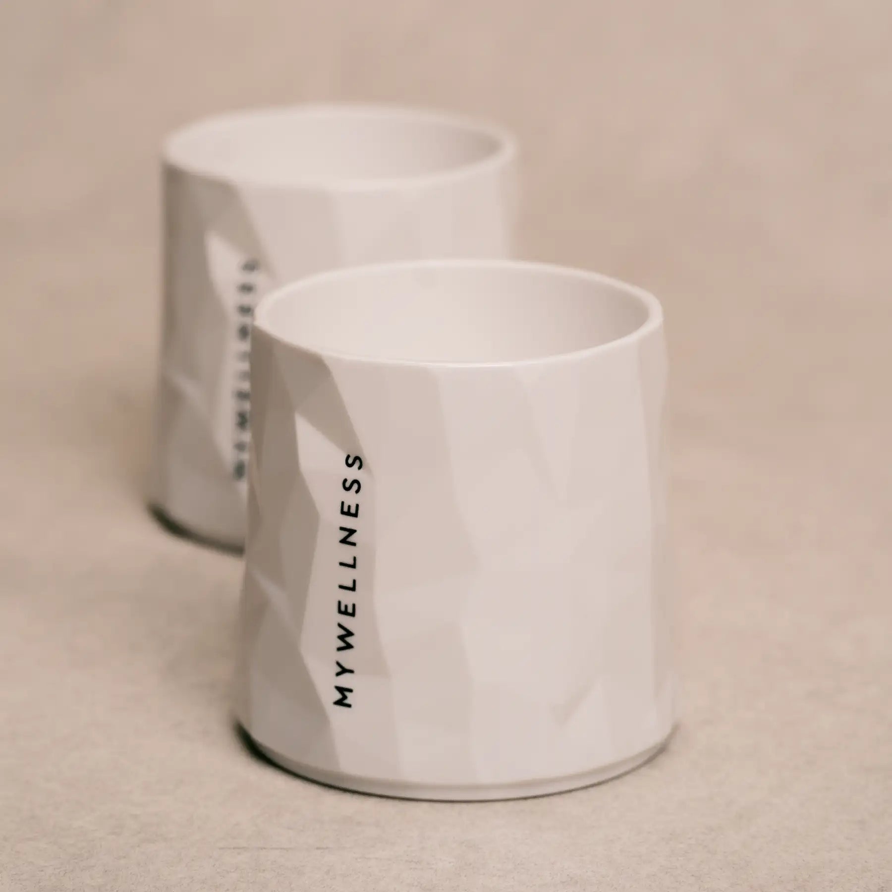 Strukturierte weiße MYWELLNESS-Becher mit klar sichtbarem Logo, minimalistisches Studiodesign.