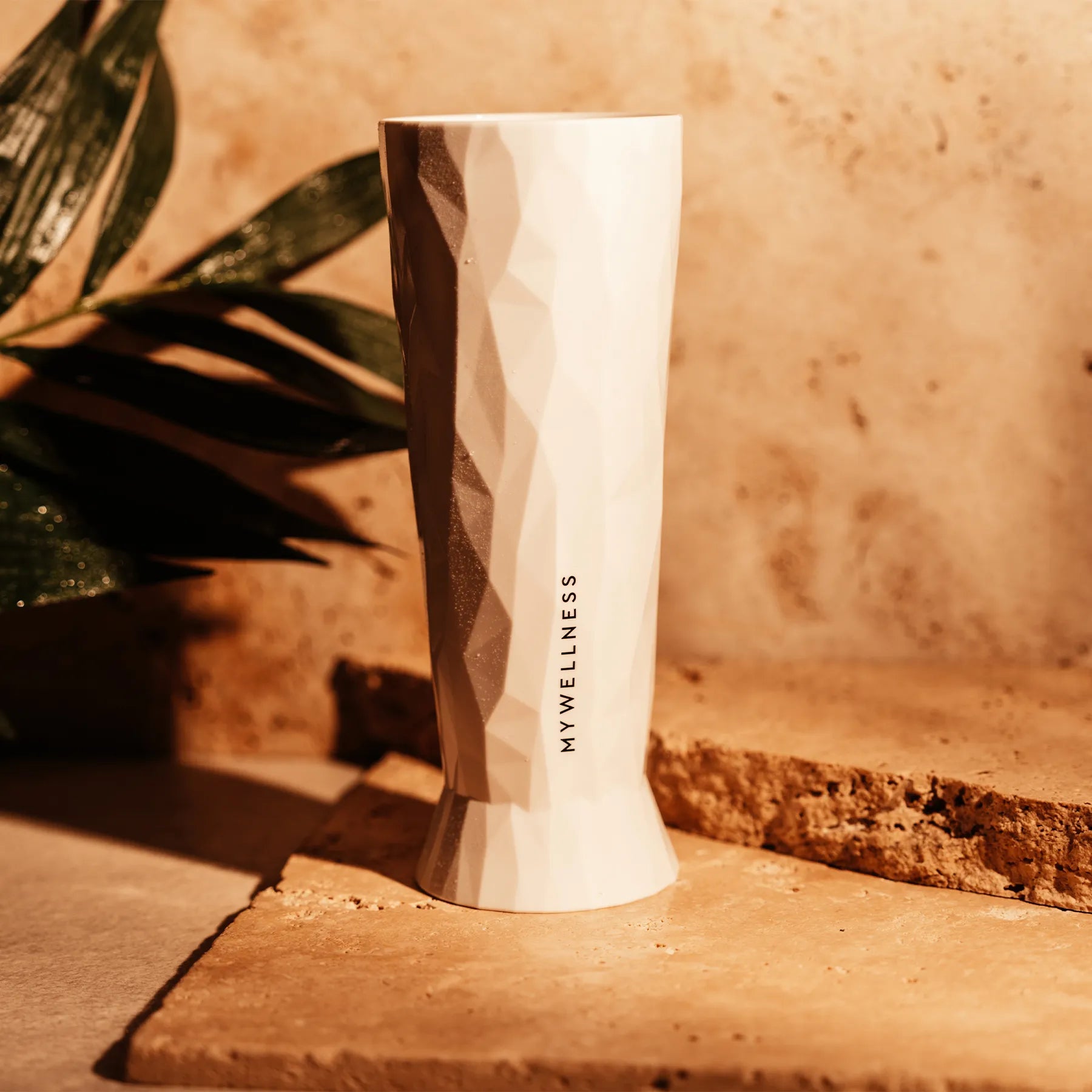 Weißes MyWellness-Bierglas mit strukturierter Oberfläche, beleuchtet von warmem Licht auf Natursteinuntergrund.