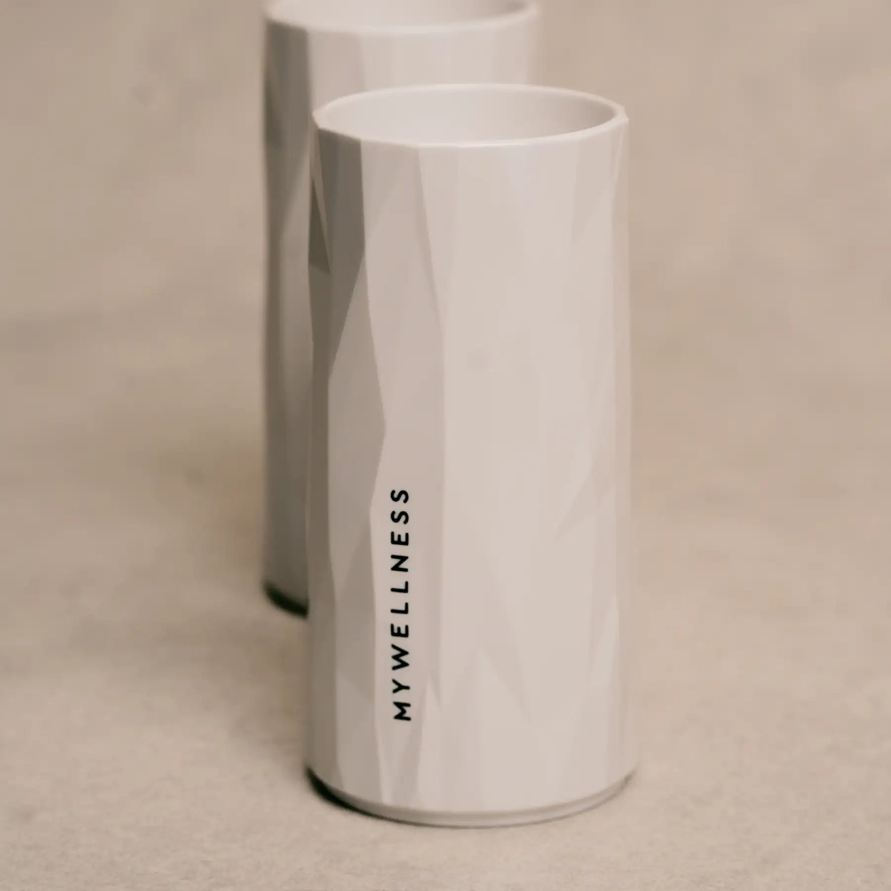 Zwei elegante weiße MYWELLNESS-Longdrinkgläser mit vertikalem Logo, Detailaufnahme im Studio.