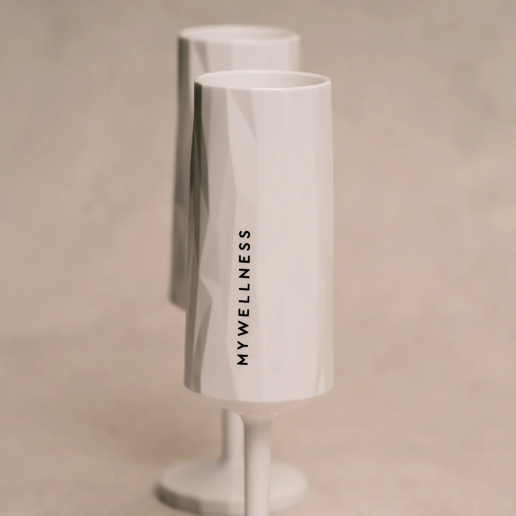 Zwei strukturierte weiße MYWELLNESS-Sektgläser mit klar sichtbarem vertikalem Logo, Studioaufnahme.